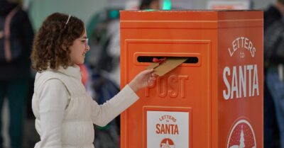 Kid putting a letter in an orange postbox in the airport